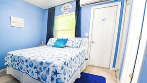 Un dormitorio con una cama, pared azul, ventana con cortinas y una puerta.