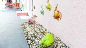 Un patio con sillas de colores, un aplique de luz en la pared y esculturas decorativas de peces.