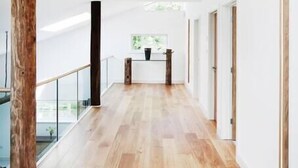A spacious hallway with wooden flooring, white walls, and a glass railing on one side. - The Pole Barn -Stunning High Spec Barn Conversion (Winford)