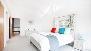 A modern bedroom with a large bed, a nightstand, a window with curtains, and a door leading to another room. - The Pole Barn -Stunning High Spec Barn Conversion (Winford)