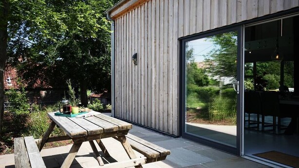 A wooden picnic table outside a modern building with a glass door. - The Pole Barn -Stunning High Spec Barn Conversion (Winford)