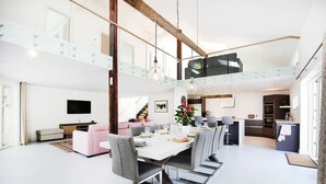 A spacious living area with a high ceiling, a dining table with chairs, a sofa, and a television. - The Pole Barn -Stunning High Spec Barn Conversion (Winford)