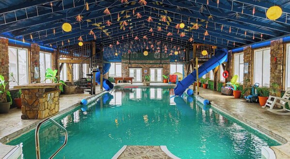 An indoor swimming pool with slides, stone walls, and potted plants.