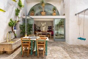 Un espace extérieur aménagé pour les repas, avec une table et des chaises, un bac à fleurs en béton et des plantes en pot.