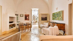 A spacious room with a high arched ceiling, a dining area with a table and chairs, a sofa, a cabinet, and a painting on the wall.