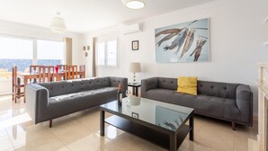 A modern living room with a grey sectional sofa, a glass coffee table, and a dining area with wooden chairs and a table. - Villa Diego - Five Bedroom Villa, Sleeps 10 (Puerto del Carmen)