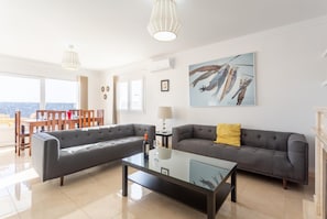A modern living room with a grey sectional sofa, a glass coffee table, and a dining area with wooden chairs and a table. - Villa Diego - Five Bedroom Villa, Sleeps 10 (Puerto del Carmen)