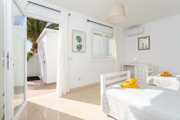 Un dormitorio luminoso con dos camas, una ventana y una puerta que da a un balcón.