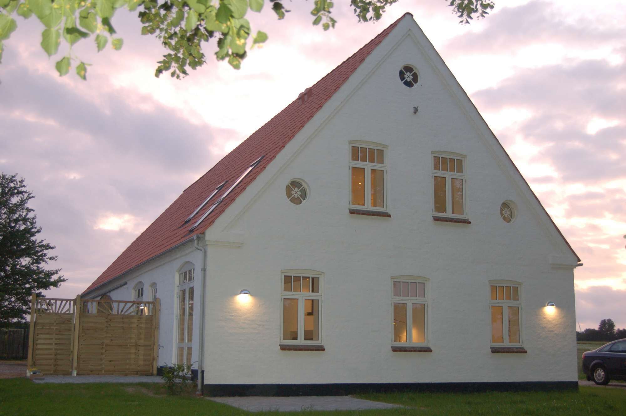 A white building with a red roof, multiple windows, and a wooden fence in front.