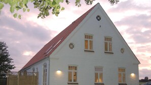 Een wit gebouw met een rood dak, meerdere ramen en een houten hek er voor.