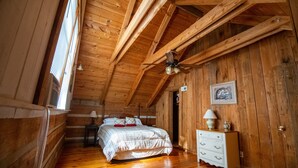 Ein Schlafzimmer in einer Holzhütte mit Bett, Schminktisch und Deckenventilator.