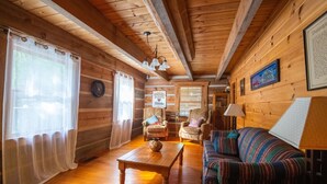 Ein gemütliches Blockhaus-Interieur mit Holzwänden, einer Couch, einem Tisch und einem Sessel.