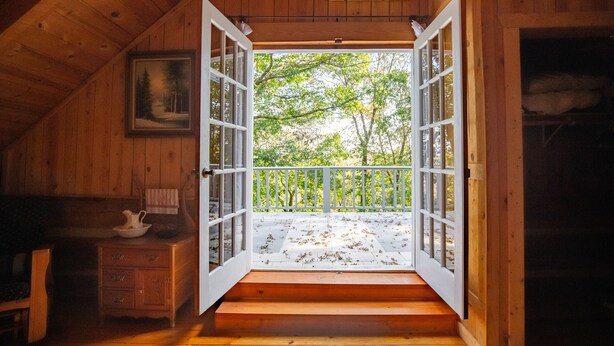 Eine Holzhütte mit offener Tür, die auf einen Balkon mit Blick ins Grüne führt.