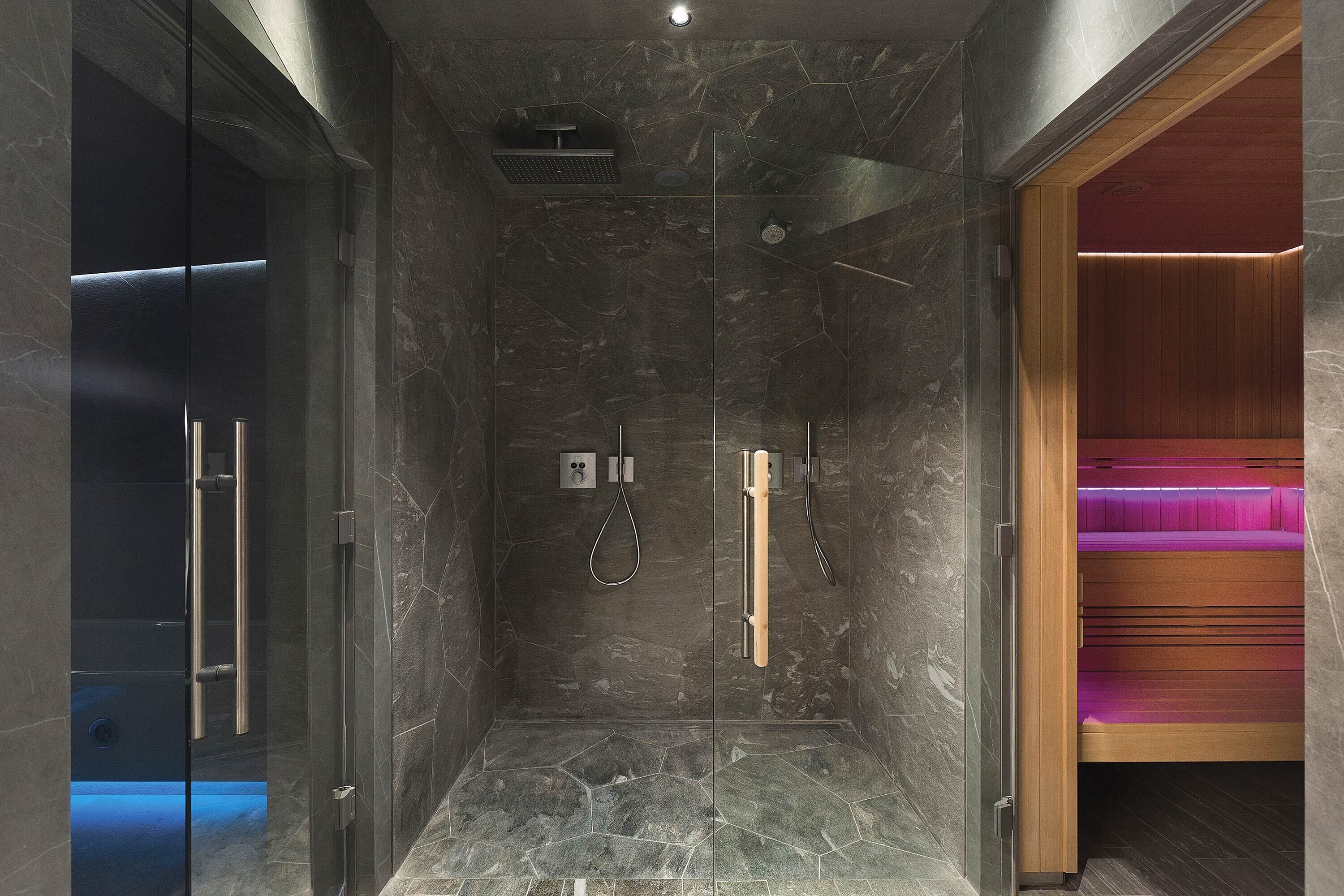 A modern shower area with a glass door, a wooden bench, and a built-in massage chair.