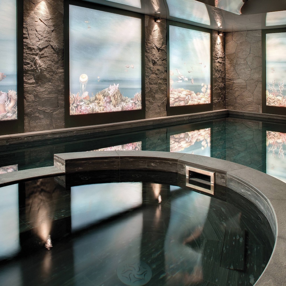 A modern indoor swimming pool with a stone wall and large windows.