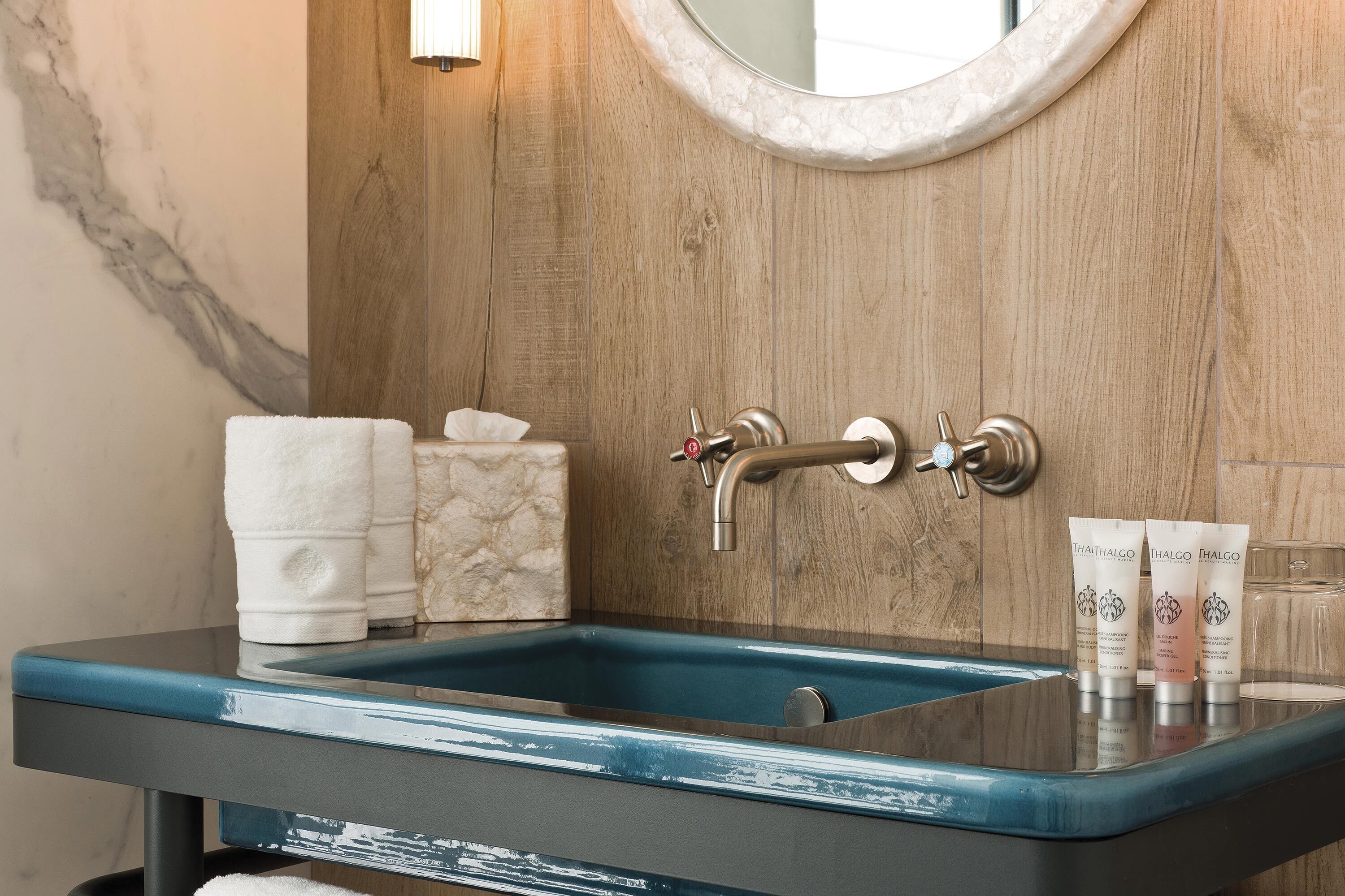 Un baño con pared de madera, pared con azulejos de mármol, un lavabo azul y dos toallas blancas.