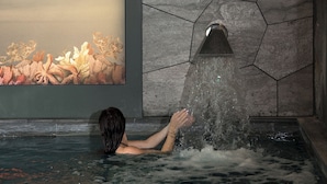 A person in a bathtub with water jets, a wall with hexagonal tiles, and a mural of underwater scenery. - La Demeure Montaigne (Paris)
