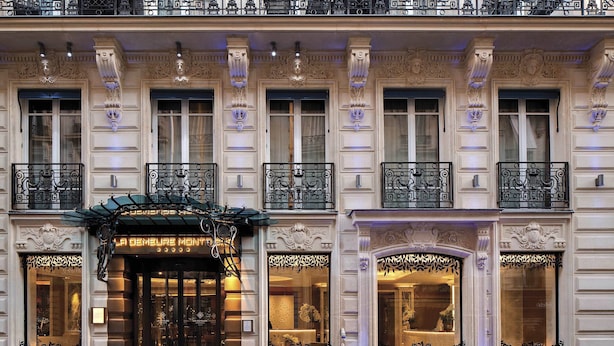 A historic building with ornate iron balconies, large windows, and a prominent entrance with a glass door. - La Demeure Montaigne (Paris)