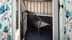 A balcony with a chair, a view of the Eiffel Tower, and blue floral curtains. - La Demeure Montaigne (Paris)