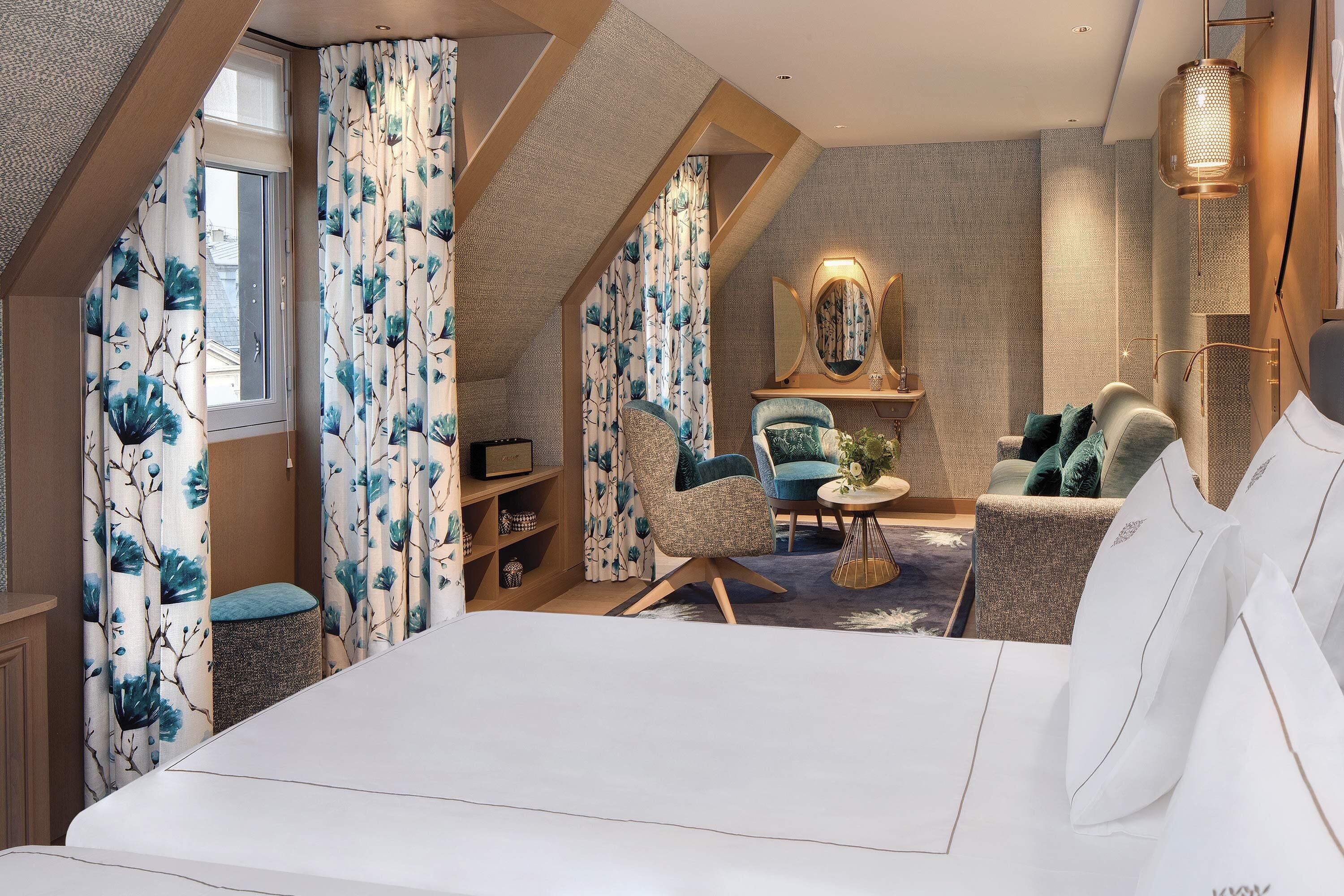 A bedroom with a large bed, a seating area with a chair and a small table, a mirror, and a decorative lamp.