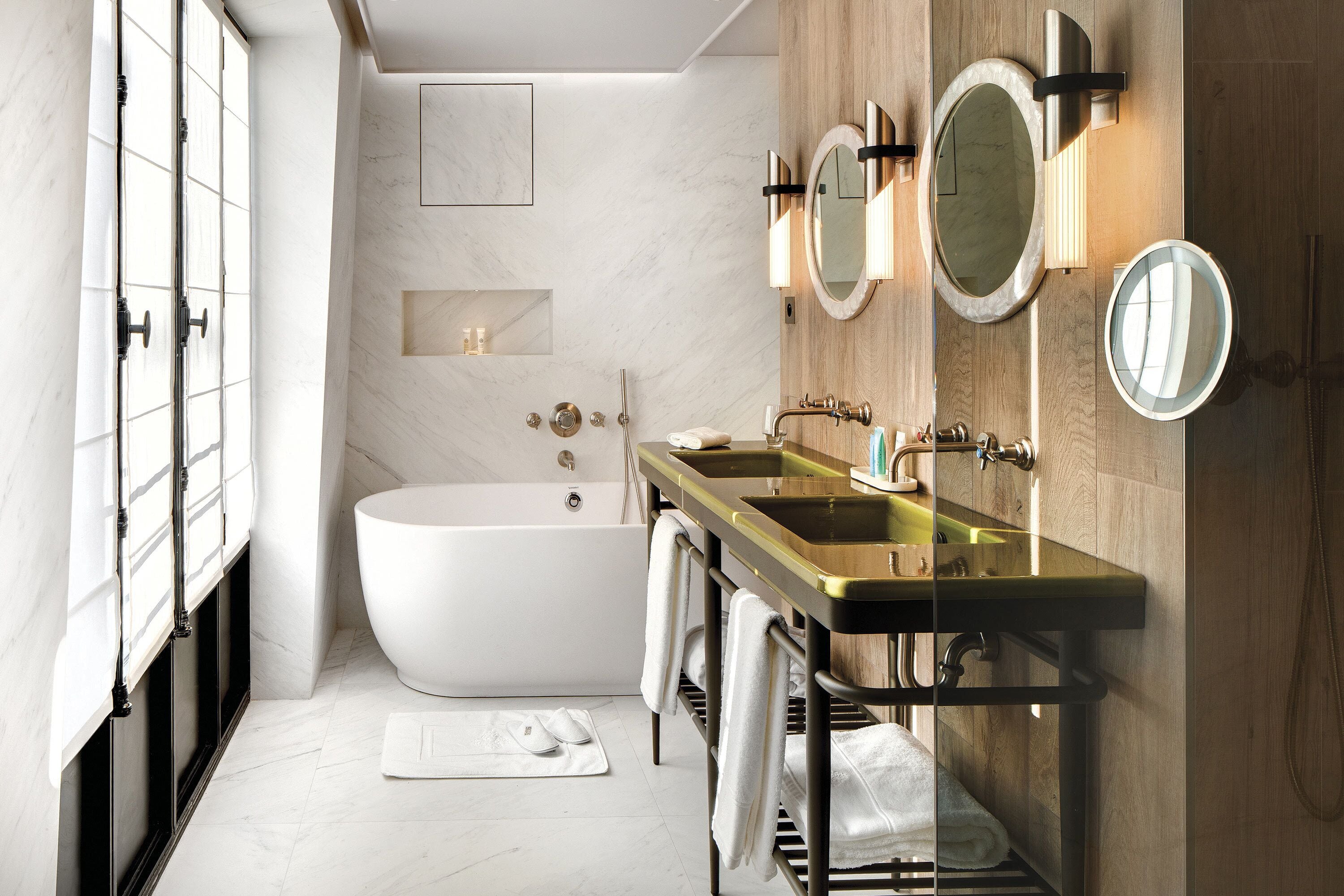 A modern bathroom with a freestanding bathtub, a vanity with a gold sink, and two wall-mounted mirrors.