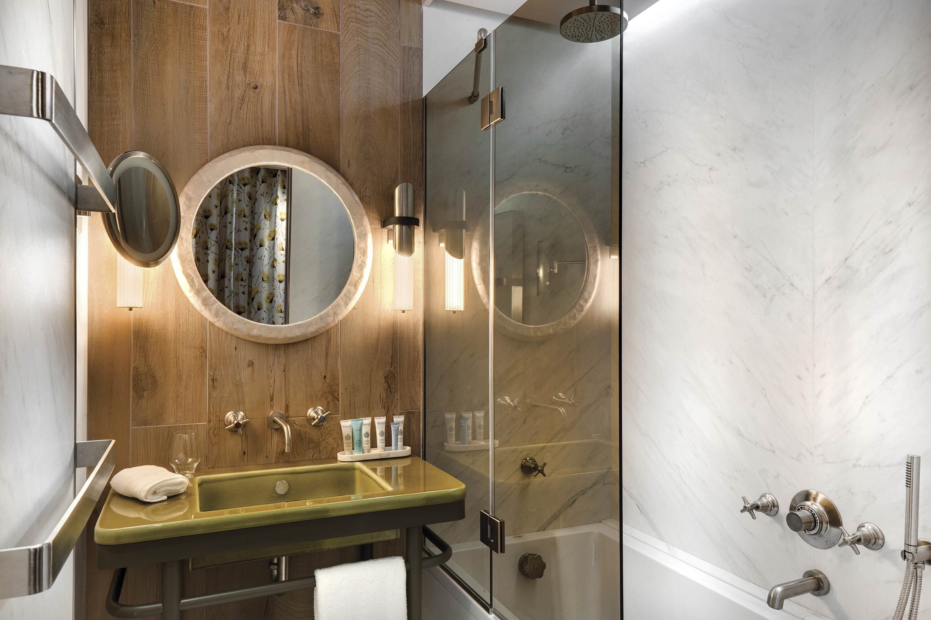 A modern bathroom with a wooden vanity, a round mirror, and a glass-enclosed shower.