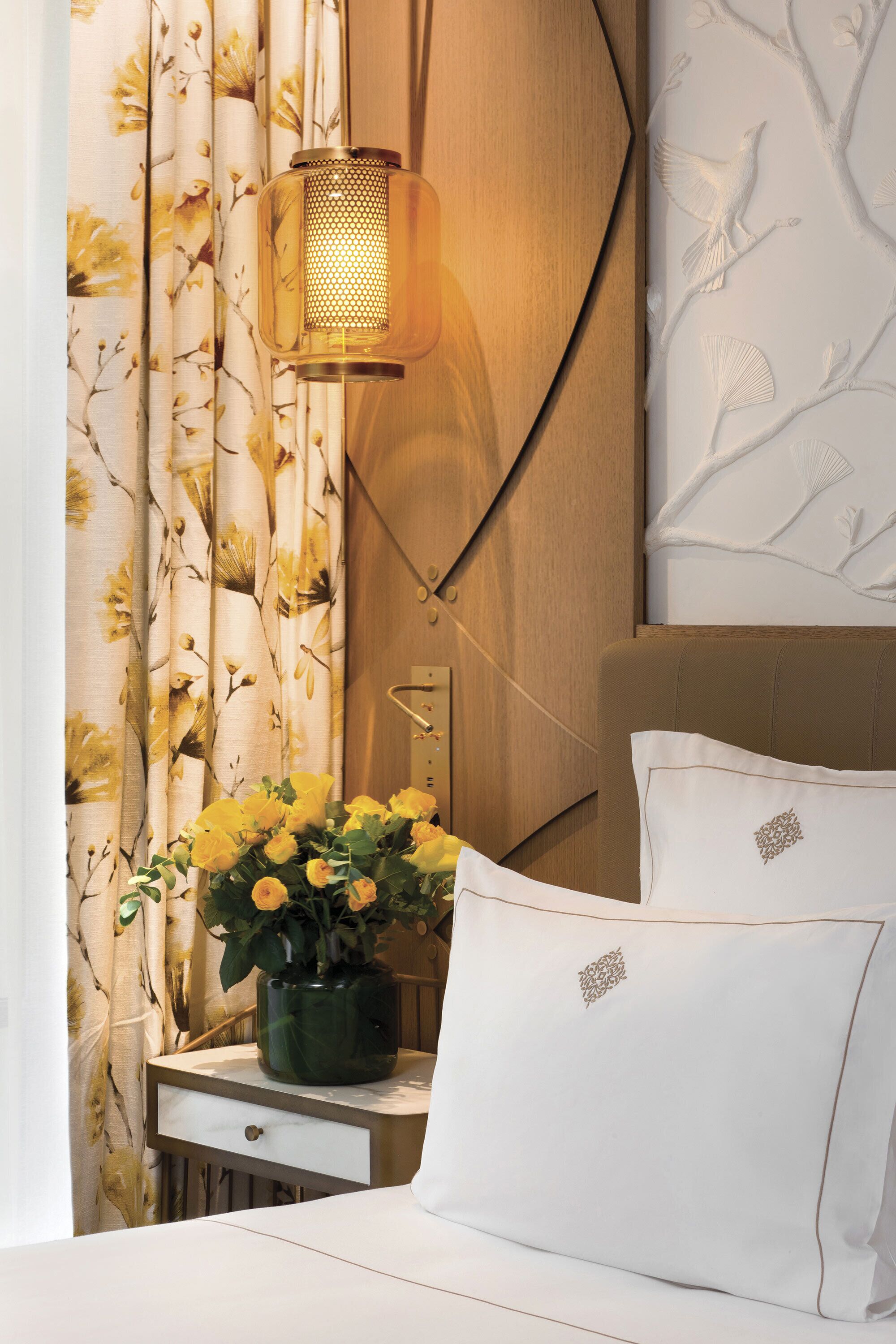 Une chambre à coucher bien rangée, avec un lit, une table de chevet dotée d’une lampe et un rideau à motifs floraux.