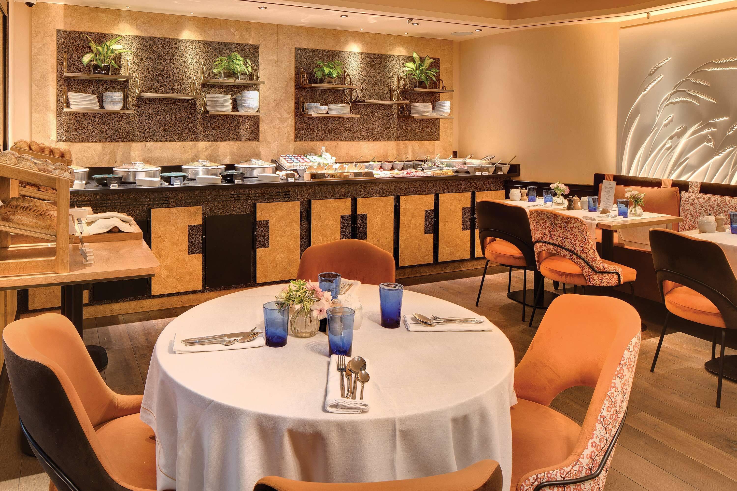 Un restaurant doté d’un buffet, de tables rondes avec des chaises orange et d’étagères décoratives murales.