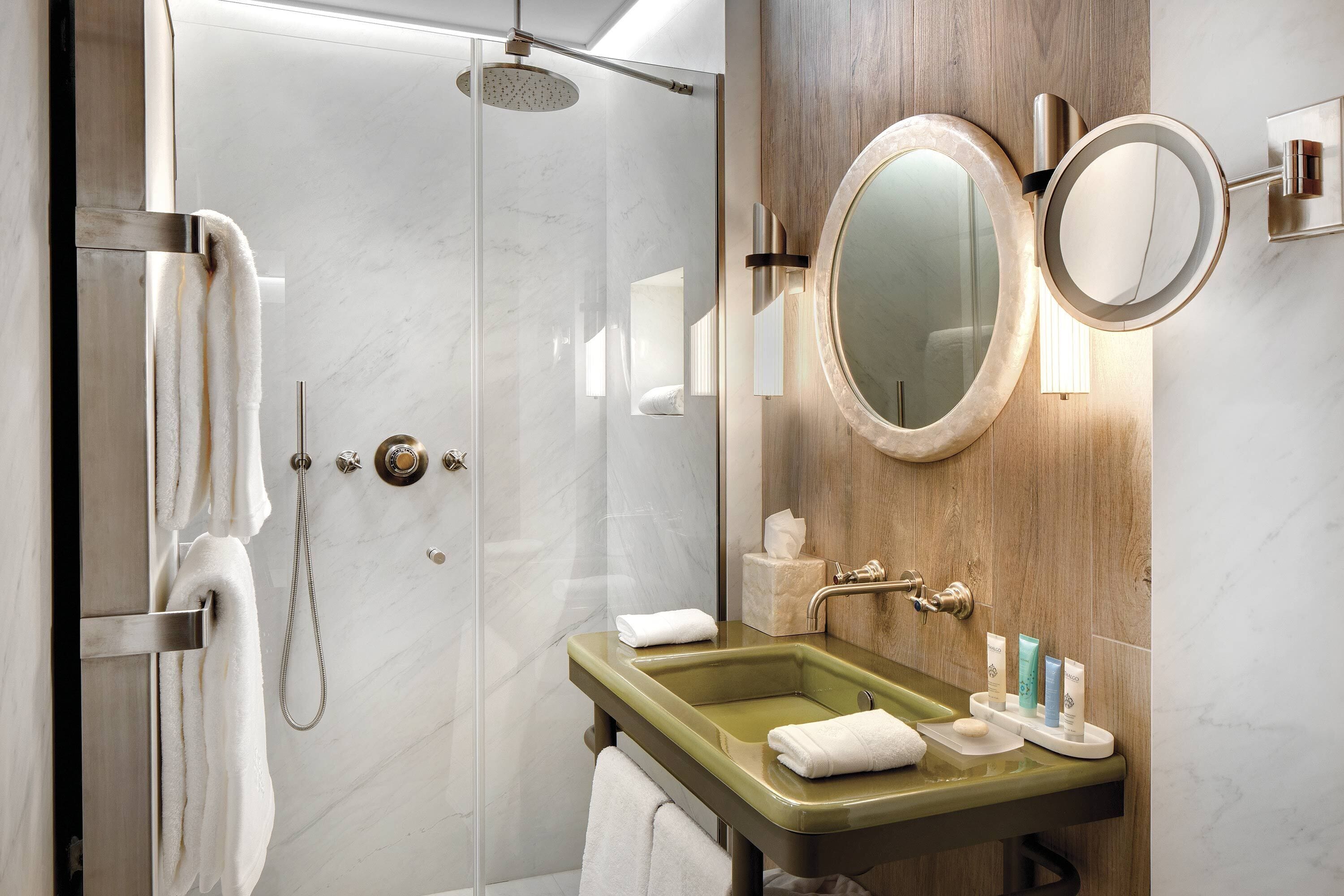 A modern bathroom with a glass-enclosed shower, a green sink, and two wall-mounted mirrors.