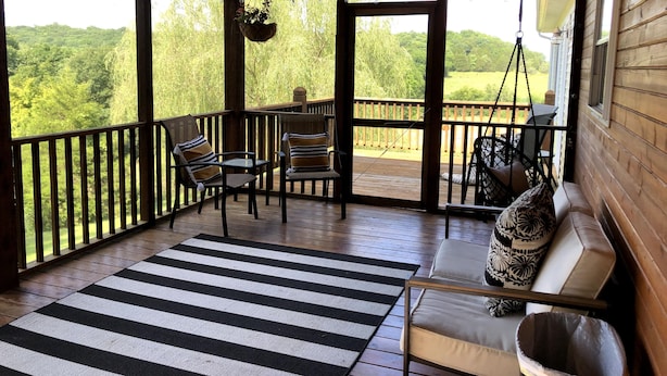 Eine Holzterrasse mit einem schwarz-weiß gestreiften Teppich, einer gepolsterten Bank und Stühlen.