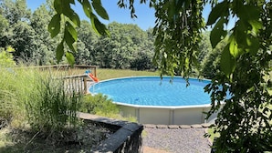Ein rechteckiger Pool, umgeben von einer Steinmauer, mit einem Holzdeck und einer Rutsche, die ins Wasser führt.