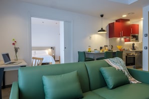 Une chambre d’hôtel moderne avec un canapé vert, une table à manger et un coin cuisine doté de meubles rouges.