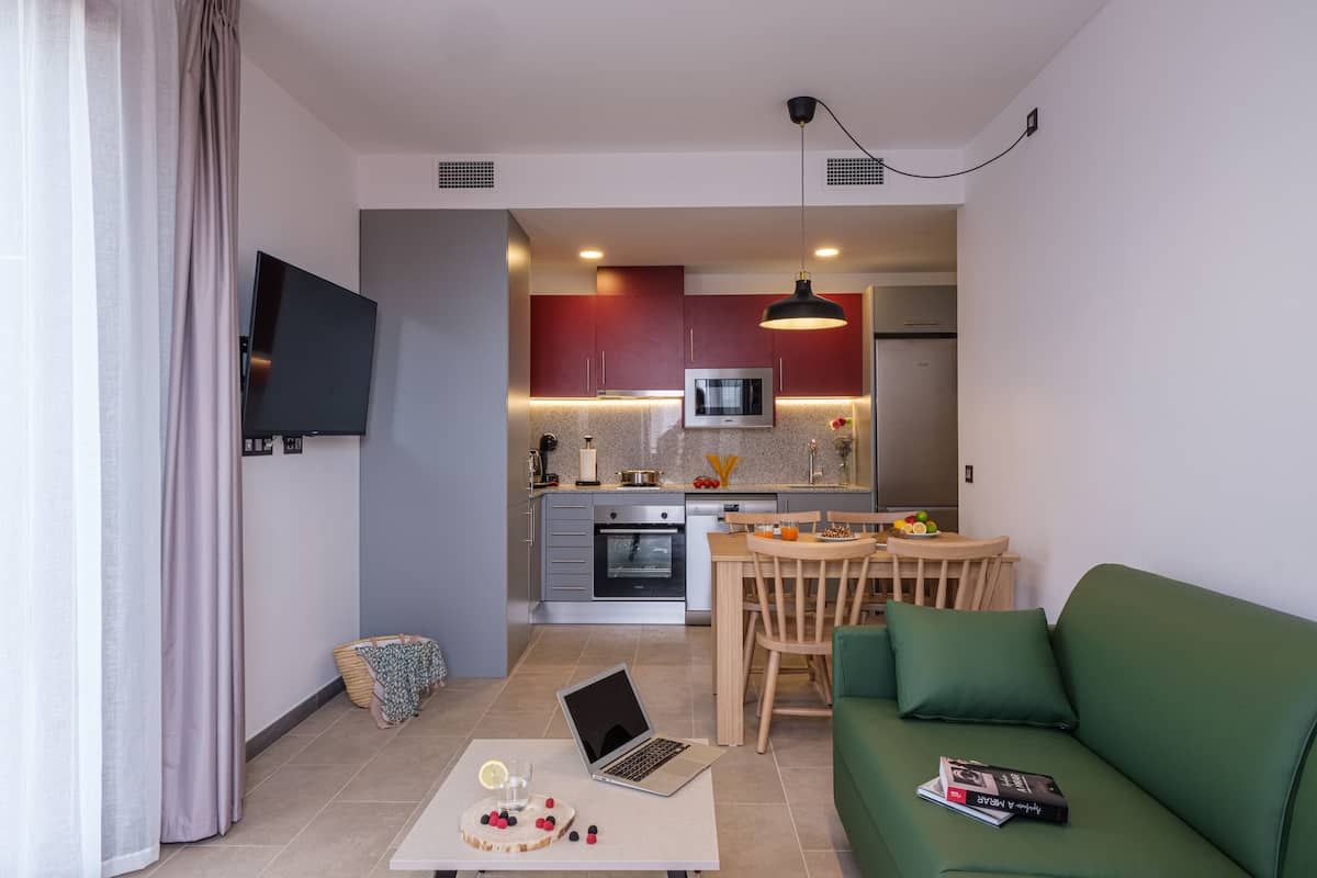 Uma sala de estar moderna com um sofá verde, uma mesa de jantar de madeira e um laptop sobre uma mesinha.