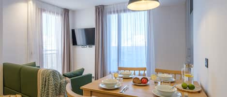 Un comedor con una mesa de madera dispuesta para dos personas, un sofá verde y un televisor montado en la pared.