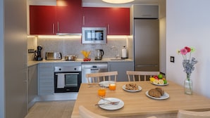 Una cocina moderna con armarios rojos, electrodomésticos de acero inoxidable y una mesa de comedor de madera dispuesta con platos, vasos y un florero con flores.