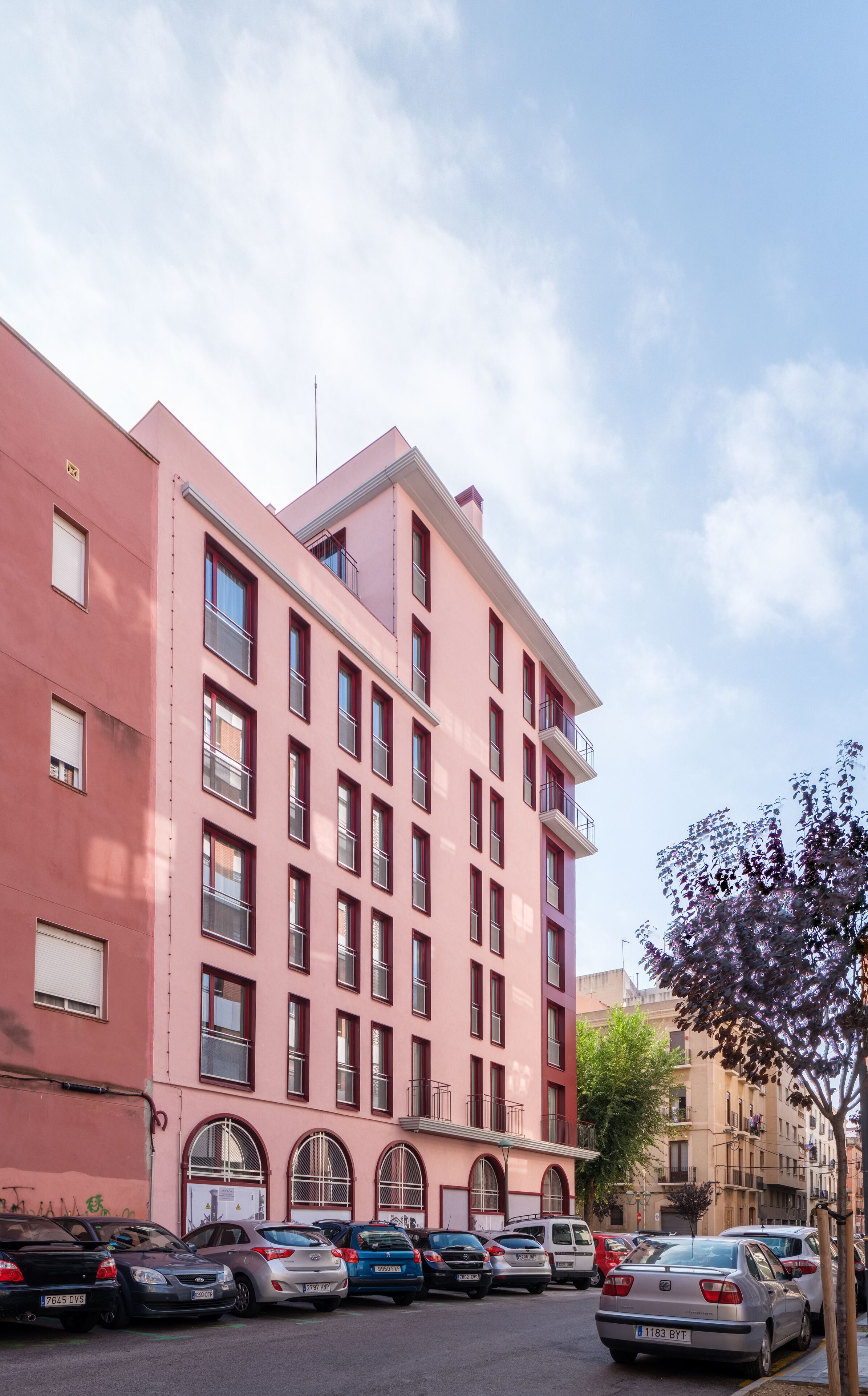 Un edificio rosa de varios pisos con una fila de coches estacionados al frente.