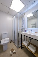 Un baño moderno con ducha envuelta en vidrio, un inodoro blanco, un lavabo con espejo y un estante con toallas dobladas.