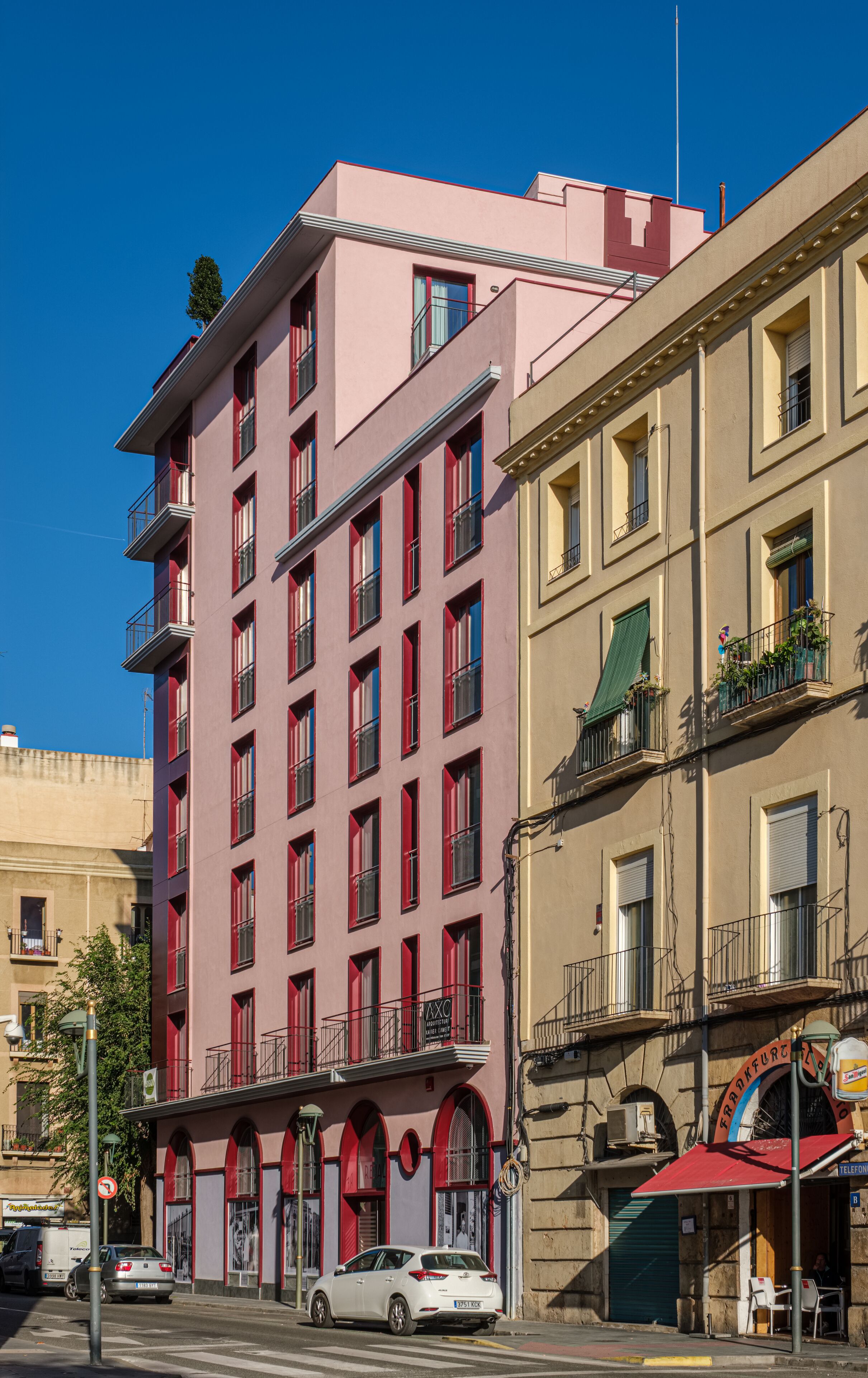 A multi-story building with a red facade, balconies, and a visible sign indicating it is a hotel.