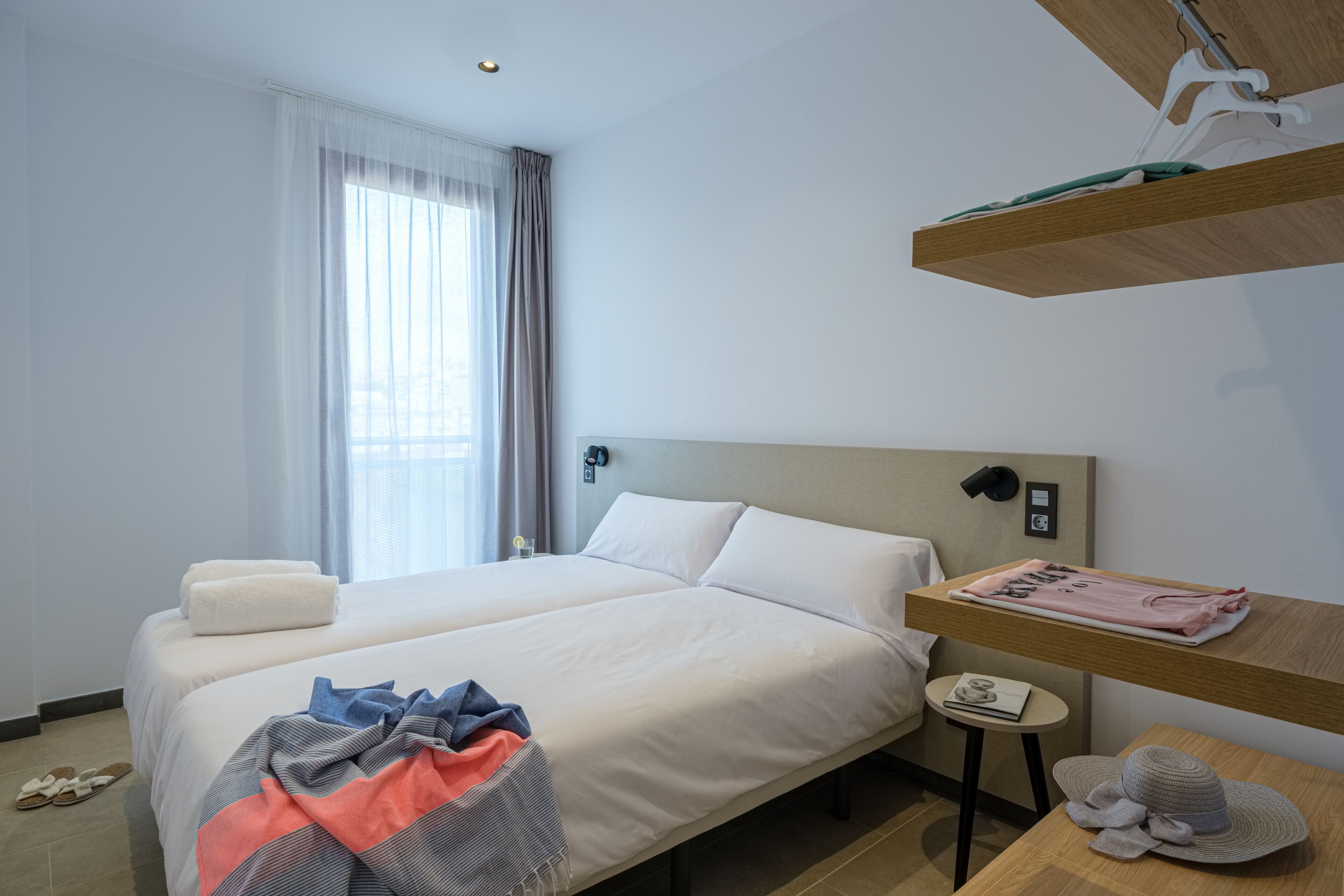 Una camera d'albergo con un letto grande, un comodino, una mensola sospesa e una finestra con tende.