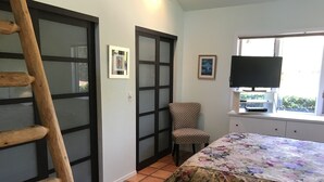 A room with a bed, a chair, a TV, and a window with blinds. - Uptown Boho Comfort - Uptown Sedona - Beautiful 3 Bedroom Home w/a View (Sedona)