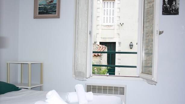 A bedroom with a bed, a window with a view of a building, a bedside table, and a wall-mounted light fixture. - Appartement champêtre - Déconnexion assurée (Poitiers)