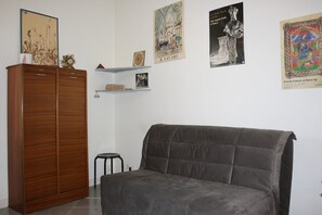 Une pièce avec un canapé gris foncé, une armoire en bois et un petit tabouret. Trois œuvres d’art encadrées sont accrochées au mur.