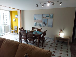 Ein Essbereich mit Tisch für vier Personen, umgeben von Holzstühlen, und eine Couch im Vordergrund.