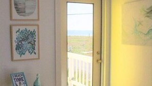 Una habitación con una puerta que da a un balcón, una pequeña mesa con un letrero y dos cuadros en la pared.