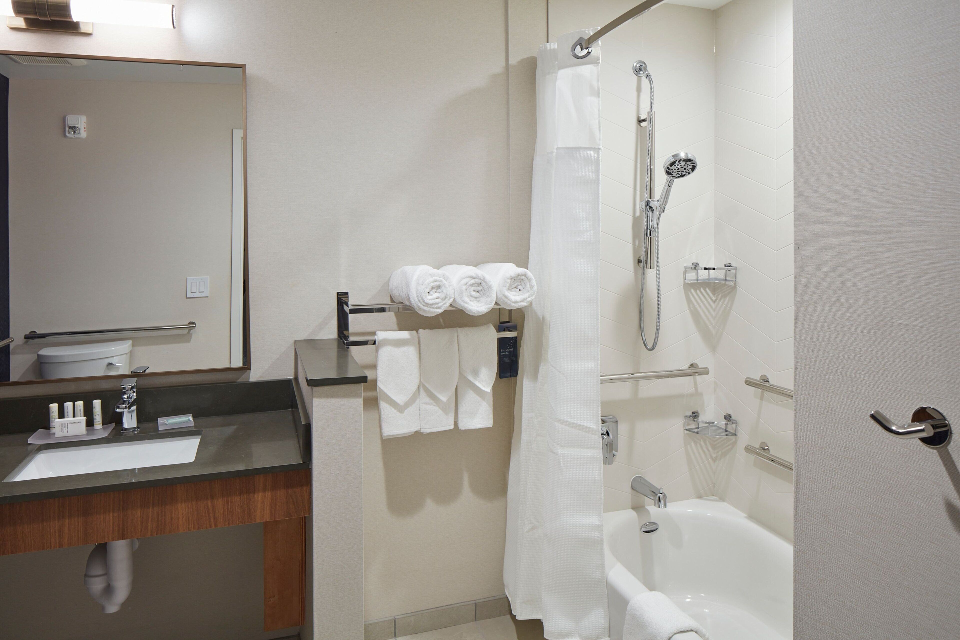 Een moderne badkamer met een wastafel, spiegel, handdoekhouder, douche en bad.