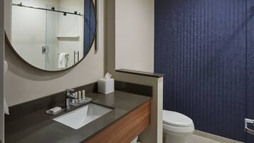 A bathroom with a round mirror, a sink with toiletries, a toilet, and a towel rack.