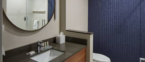 Een badkamer met een ronde spiegel, een wastafel met toiletartikelen, een toilet en een handdoekhouder.