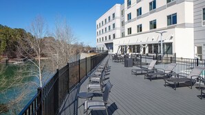 A deck with outdoor seating overlooking a body of water, adjacent to a building with multiple windows.