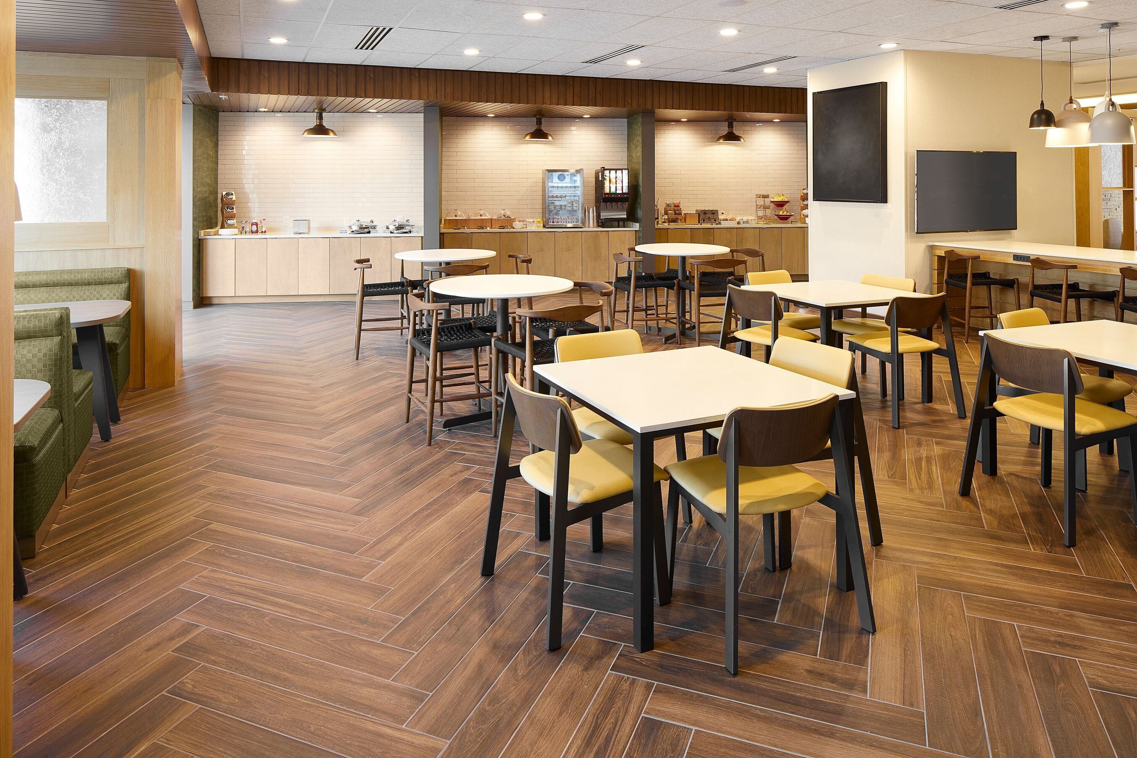 Um restaurante moderno com piso de madeira, mesas redondas e cadeiras amarelas.