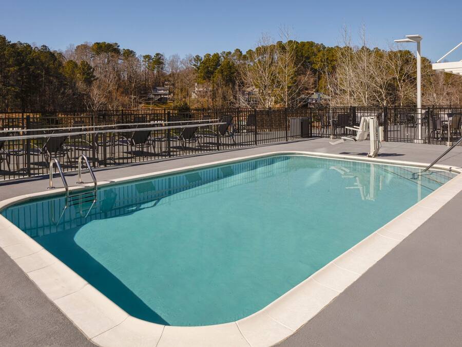 A rectangular pool with a metal railing, surrounded by a fence and outdoor seating.